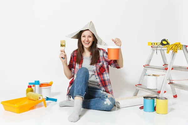 Γυναίκα με καπέλο εφημερίδα κάθεται στο πάτωμα με πινέλο, χρώμα μπορεί, μέσα για διαμέρισμα ανακαίνιση που απομονώνονται σε λευκό φόντο. Ταπετσαρία, αξεσουάρ για την κόλληση, εργαλεία ζωγραφικής. Επισκευή concept home — Φωτογραφία Αρχείου