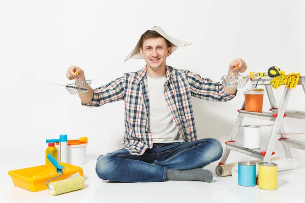 Homem feliz em chapéu de jornal detém supermercado de metal mercearia cestas para fazer compras. Instrumentos para renovação apartamento isolado em fundo branco. Acessórios papel de parede ferramentas de pintura. Conceito de reparação — Fotografia de Stock