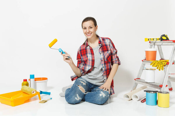 Woman in casual clothes sitting on floor with paint roller, instruments for renovation apartment isolated on white background. Wallpaper, accessories for gluing, painting tools. Repair home concept.