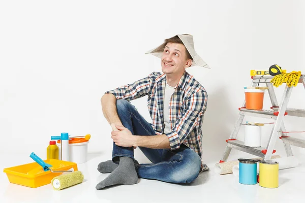 Diversão feliz sorridente homem em chapéu de jornal sentado no chão com instrumentos para renovação apartamento quarto isolado no fundo branco. Papel de parede, acessórios de colagem, ferramentas de pintura. Reparação home concept . — Fotografia de Stock