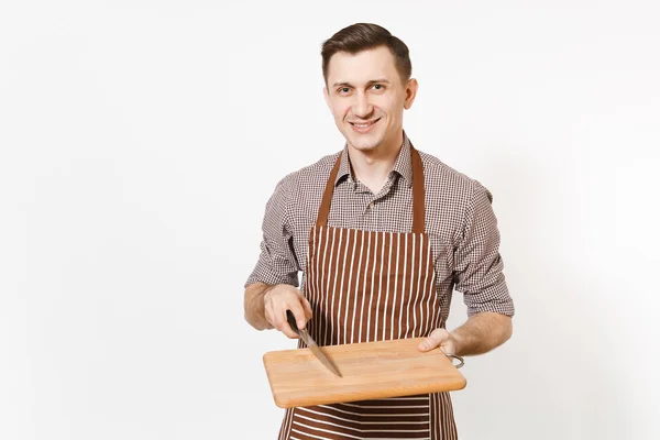 Joven hombre sonriente chef o camarero en delantal marrón rayado, camisa con tabla de cortar de madera, cuchillo aislado sobre fondo blanco. Hombre ama de llaves o empleada doméstica. Trabajadora doméstica para publicidad . —  Fotos de Stock