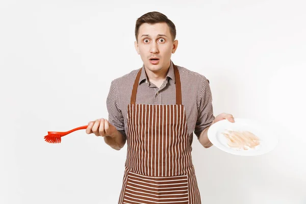 Веселий шеф-кухар у смугастому коричневому фартусі, сорочка тримає миття білої круглої порожньої брудної тарілки з червоною щіткою для миття посуду ізольованої на білому тлі. Чоловік-домогосподарка, працівник або домашній працівник — стокове фото