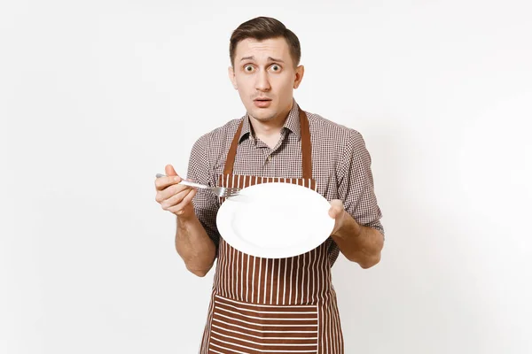 Homem chef ou garçom em avental marrom listrado, camisa segurando branco rodada placa clara vazia, garfo isolado no fundo branco. Empregada doméstica ou doméstica. Doméstico espaço cópia trabalhador para publicidade — Fotografia de Stock