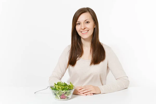 Mujer joven sentada a la mesa con ensalada de hojas verdes en cuenco de vidrio aislado sobre fondo blanco. Nutrición adecuada, comida vegetariana, estilo de vida saludable, concepto de dieta. Área de publicidad con espacio de copia —  Fotos de Stock