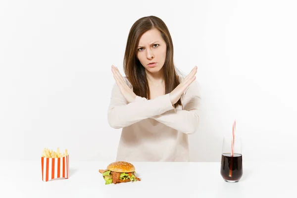 Eine strenge Frau zeigt Stopp-Geste am Tisch mit Burger Pommes Cola in Glasflasche auf weißem Hintergrund. richtige Ernährung oder klassisches amerikanisches Fast Food. Werbefläche mit Kopierfläche. — Stockfoto