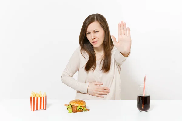 Choroby kobieta rękę na ból brzucha, ból brzucha przy stole z burger, frytki, cola w szklanej butelce na białym tle. Prawidłowe odżywianie lub klasyczny amerykański fast food. Miejsce. — Zdjęcie stockowe