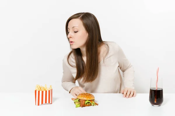 Hermosa joven sentada a la mesa con hamburguesa, papas fritas, cola en botella de vidrio aislada sobre fondo blanco. Nutrición adecuada o comida rápida clásica americana. Área de publicidad con espacio de copia . —  Fotos de Stock