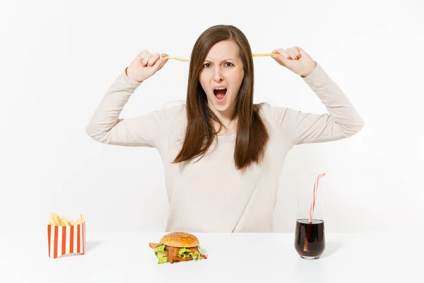 Ontevreden vrouw aan tafel met verschillende soorten aardappelen, friet, hamburger, cola in fles geïsoleerd op een witte achtergrond. Goede voeding of Amerikaanse klassieke fastfood. Gebied met kopie ruimte. — Stockfoto