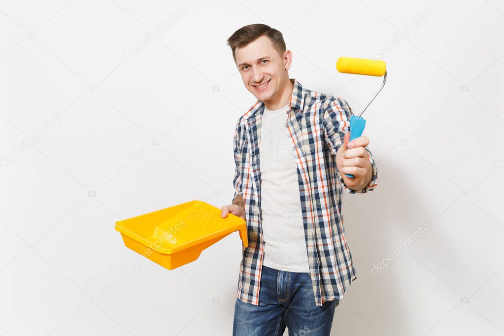 Young smiling handsome man in casual clothes holding paint tray and paint roller for wall painting isolated on white background. Instruments, tools for renovation apartment room. Repair home concept.