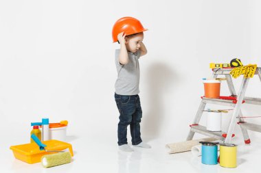 Beyaz arka plan üzerinde izole yenileme daire için aygıtlar ile turuncu koruyucu kask içinde küçük bir çocuk. , Duvar kağıdı yapıştırma aksesuarları, boyama araçlarını. Onarım ev. Ebeveynlik, çocukluk kavramı