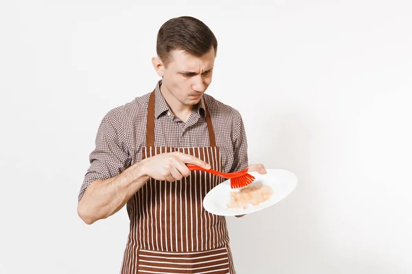 Divertente cuoco uomo in grembiule marrone rigato, camicia tiene lavaggi bianco rotondo piatto sporco vuoto con spazzola rossa per lavare i piatti isolati su sfondo bianco. Casalinga, domestica o domestica — Foto Stock