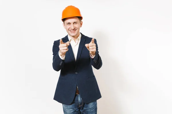 Jovem bonito sorridente empresário em terno escuro, construção protetora capacete laranja apontando dedos indicadores na câmera isolada no fundo branco. Trabalhador masculino para propaganda. Conceito de negócio . — Fotografia de Stock