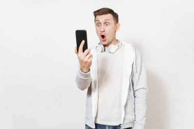 Genç yakışıklı adam öğrenci tişört içinde şok ve beyaz arka plan üzerinde izole cep telefonunda sürpriz yüzünü ışık kazak boynuna kulaklıklarla alır. İletişim, duyguların kavramı