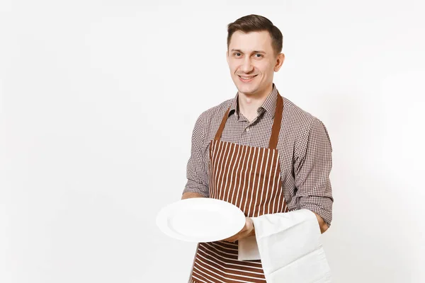 Jonge man chef-kok of kelner in gestreepte bruine schort, shirt met witte ronde lege duidelijk plaat, handdoek servet geïsoleerd op een witte achtergrond. Mannelijke huishoudster of houseworker. Huishoudelijk werker, kopie ruimte. — Stockfoto