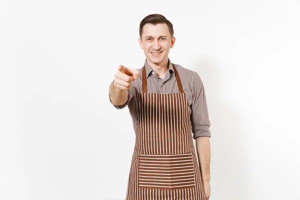 Young smiling man chef or waiter pointing finger on camera in striped brown apron, shirt isolated on white background. Male housekeeper or houseworker looking camera. Domestic worker for advertisement — Stock Photo, Image