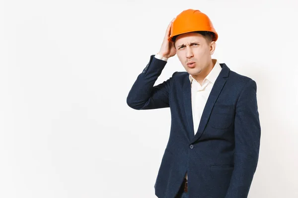 Jovem bonito empresário preocupado em terno escuro, capacete laranja construção protetora mantendo a mão na cabeça isolado no fundo branco. Trabalhador masculino para propaganda. Negócio, conceito de trabalho . — Fotografia de Stock