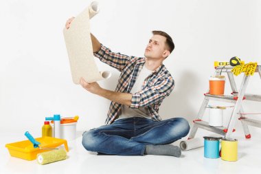 Beyaz arka plan üzerinde izole yenileme daire oda için duvar kağıdı aygıtlar gelişeceğini rulo ile katta oturan yakışıklı adam. Boyama araçlarını aksesuarları yapıştırma. Onarım ev concept. Kopya alanı