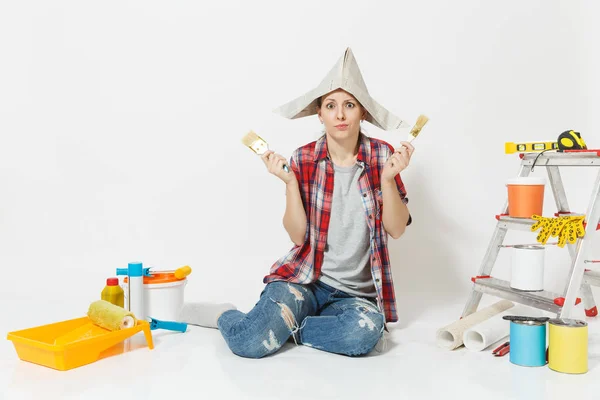 Mujer divertida en sombrero de periódico sentado en el suelo con cepillo, instrumentos para la renovación habitación del apartamento aislado sobre fondo blanco. Fondos de pantalla, accesorios para pegar, herramientas de pintura. Reparación concepto hogar . — Foto de Stock