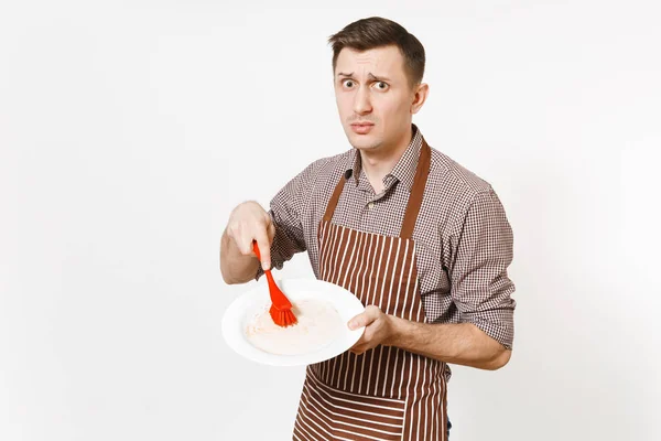 Leuk man chef-kok in gestreepte bruine schort, shirt houdt wast witte ronde lege vuile plaat met rode borstel voor afwas geïsoleerd op een witte achtergrond. Mannelijke huishoudster, houseworker of huishoudelijk werker — Stockfoto