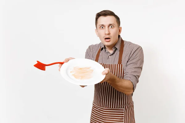 Divertente cuoco uomo in grembiule marrone rigato, camicia tiene lavaggi bianco rotondo piatto sporco vuoto con spazzola rossa per lavare i piatti isolati su sfondo bianco. Casalinga, domestica o domestica — Foto Stock