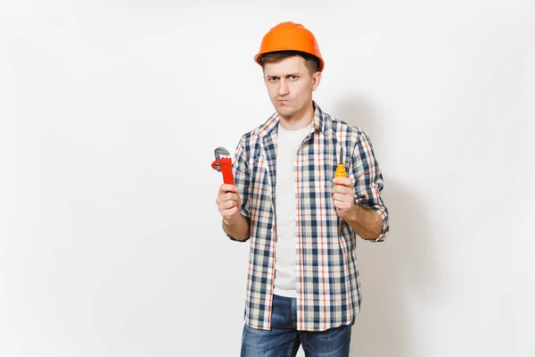 Молодий красивий чоловік у захисному помаранчевому жорсткому стані тримає іграшкову викрутку та регульований ключ ізольовано на білому тлі. Інструменти для ремонту житлової кімнати. Ремонт домашньої концепції . — стокове фото