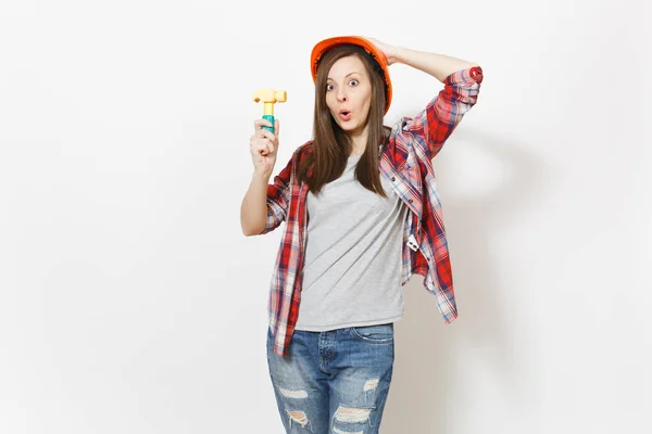 Jovem mulher chocada na construção protetora capacete laranja segurando martelo de brinquedo e agarrado à cabeça isolado no fundo branco. Instrumentos para renovação apartamento quarto. Reparação home concept . — Fotografia de Stock