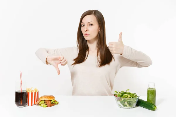 Vrouw toont duimen omhoog omlaag met groene detox smoothies, salade met glazen kom, komkommer Hamburger cola in fles geïsoleerd op een witte achtergrond. Goede voeding, gezonde levensstijl, fastfood, keuze concept. — Stockfoto