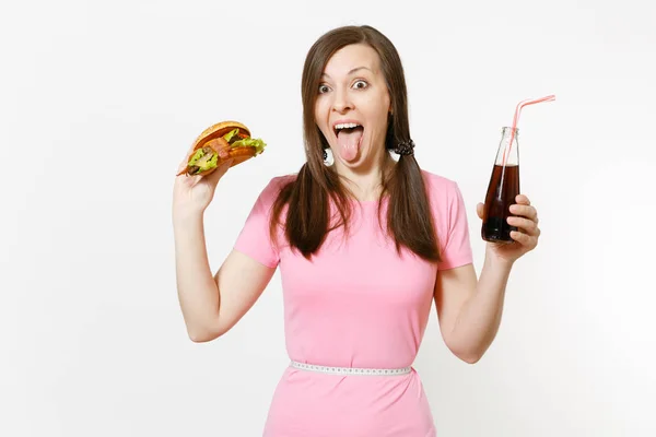 Fun young woman with tails, measuring tape at waist holding burger, cola in glass bottle isolated on white background. Proper nutrition or American classic fast food. Advertising area with copy space. — Stock Photo, Image