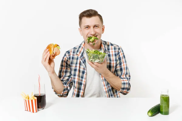 Człowiek siedzi przy stole z green detox smoothies, Sałatka w szklanej misce, ogórek, burger, frytki cola szklanki na białym tle. Prawidłowe odżywianie, zdrowy styl życia, fast food, wybór koncepcji. — Zdjęcie stockowe