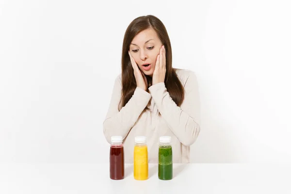 Young woman at table with green, red and yellow detox smoothies in bottles isolated on white background. Proper nutrition, vegetarian drink, healthy lifestyle, dieting concept. Area with copy space. — Stock Photo, Image