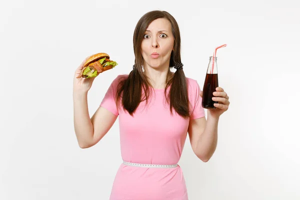 Leuke jonge vrouw met staarten, meetlint bij taille hamburger, in glazen fles cola te houden geïsoleerd op een witte achtergrond. Goede voeding of Amerikaanse klassieke fastfood. Gebied met kopie ruimte reclame. — Stockfoto