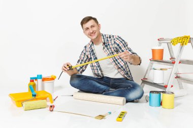 Rulo duvar kağıdı, ölçü birimi teyp, kalem, yenileme daire oda için aygıtlar ile katta oturan genç adam beyaz arka plan üzerinde izole. Aksesuarlar, boyama araçlarını yapıştırma. Onarım ev concept