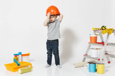 Beyaz arka plan üzerinde izole yenileme daire için aygıtlar ile turuncu koruyucu kask içinde küçük bir çocuk. , Duvar kağıdı yapıştırma aksesuarları, boyama araçlarını. Onarım ev. Ebeveynlik, çocukluk kavramı
