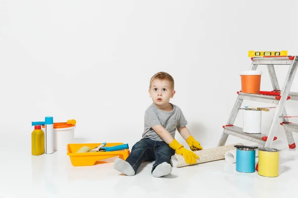 Маленький симпатичный мальчик в желтых перчатках с инструментами для ремонта квартиры изолирован на белом фоне. Обои, клеящие аксессуары, инструменты для покраски. Ремонт дома. Родительство, концепция детства . — стоковое фото