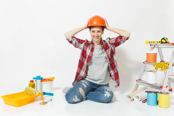 Woman in orange protective helmet sitting on floor with instruments for renovation apartment room isolated on white background. Wallpaper, accessories for gluing, painting tools. Repair home concept.