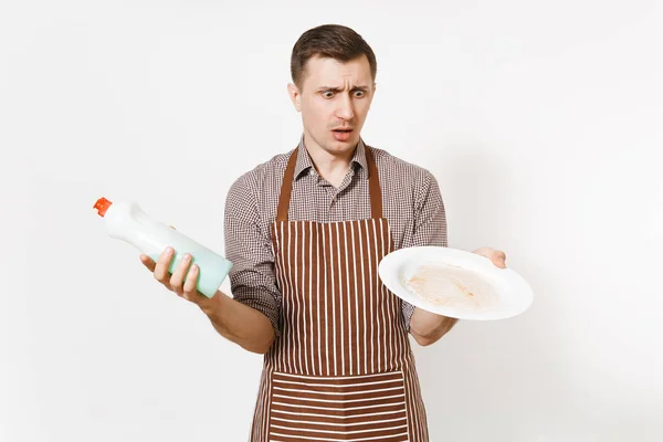 Homme en tablier brun rayé, chemise tient plaque sale ronde blanche, détergent. Laver la vaisselle avec un liquide nettoyant dans une bouteille isolée sur fond blanc. Femme de ménage, femme de ménage ou domestique . — Photo