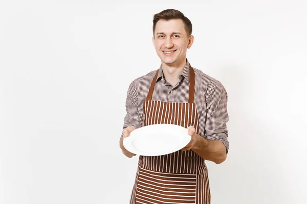 Jongeman chef-kok of kelner in gestreepte bruine schort, ronde shirt met witte lege duidelijk plaat geïsoleerd op een witte achtergrond. Mannelijke huishoudster of houseworker. Huishoudelijk werker kopie ruimte voor reclame — Stockfoto