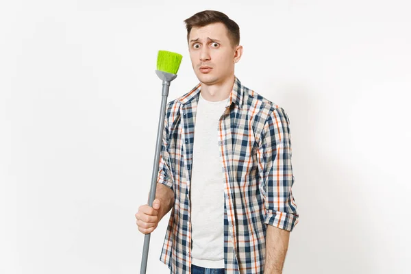 Joven y divertido ama de llaves con camisa a cuadros sosteniendo y barriendo con escoba verde aislada sobre fondo blanco. Hombre haciendo tareas domésticas. Copia espacio para la publicidad. Concepto de limpieza . — Foto de Stock