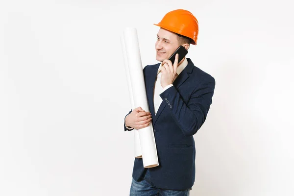 Joven hombre de negocios sonriente en traje oscuro, protector hardhat tiene planes planos, habla en el teléfono móvil y mira a un lado en el espacio de copia aislado en el fondo blanco. Trabajador masculino para publicidad . — Foto de Stock