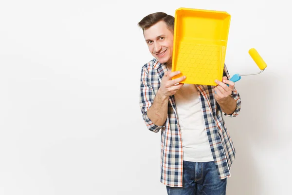 Joven hombre guapo impactado sosteniendo rodillo de pintura para la pintura de la pared y cubriendo la cara con bandeja de pintura aislada sobre fondo blanco. Instrumentos, herramientas para la renovación de la habitación del apartamento. Reparación concepto hogar . — Foto de Stock