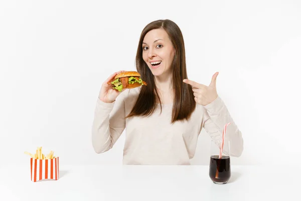 Piękna młoda kobieta siedzi przy stole z burger, frytki, cola w szklanej butelce na białym tle na białym tle. Prawidłowe odżywianie lub klasyczny amerykański fast food. Reklama obszar z miejsca kopii. — Zdjęcie stockowe