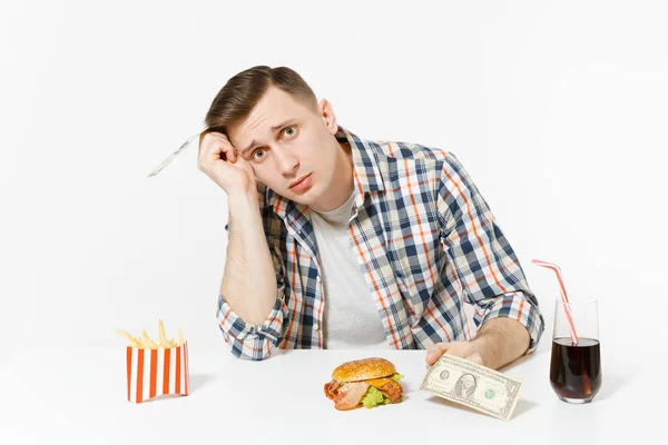 Szegény, szomorú ember ül az asztal két dollár számlák, hamburger, sült krumpli, cola pohár elszigetelt fehér background. Megfelelő táplálkozás, vagy a klasszikus amerikai gyorsétterem. Hirdetés terület másol hely. — Stock Fotó