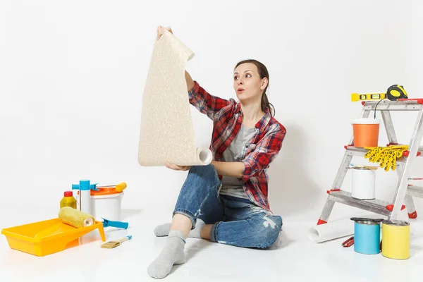 Γυναίκα σε casual ρούχα που κάθεται στο πάτωμα με εκτυλίχθηκε ρολό ταπετσαρία μέσα για διαμέρισμα ανακαίνιση που απομονώνονται σε λευκό φόντο. Αξεσουάρ για την κόλληση εργαλεία. Αρχική έννοια αντίγραφο χώρου επισκευής — Φωτογραφία Αρχείου