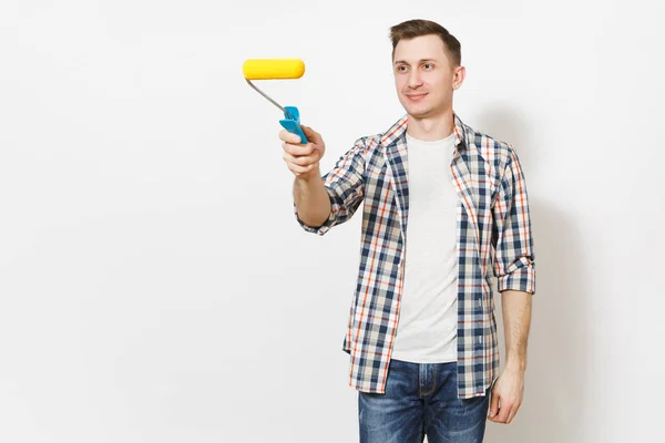 Joven hombre guapo sonriente en ropa casual apuntando rodillo de pintura para la pintura de pared en el espacio de copia aislado sobre fondo blanco. Instrumentos, herramientas para la renovación de la habitación del apartamento. Reparación concepto hogar . — Foto de Stock