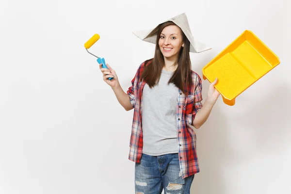 Lachende mooie jongedame in krant hoed roller voor muur schilderen en verf lade geïsoleerd op een witte achtergrond te houden. Instrumenten, tools voor renovatie appartement kamer. Reparatie home concept. — Stockfoto