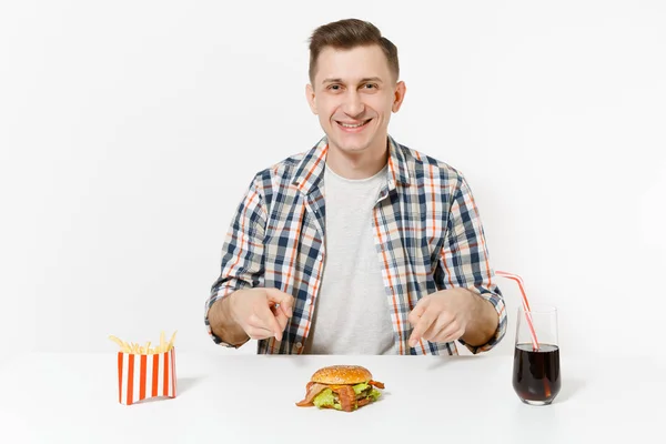 Csinos, fiatal férfi ing, hamburger, sült krumpli, cola pohár elszigetelt fehér background asztalnál ül. Megfelelő táplálkozás, vagy a klasszikus amerikai gyorsétterem. Hirdetés terület másol hely. — Stock Fotó