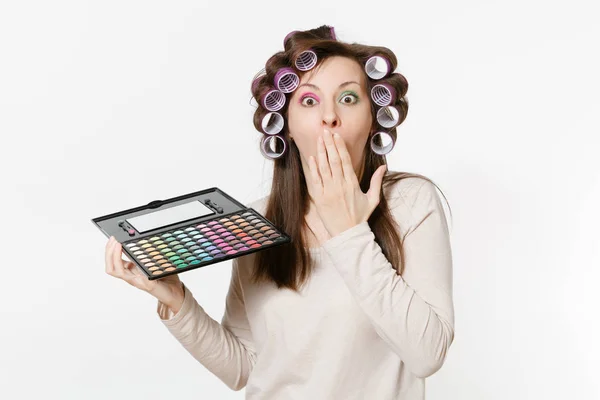 Mujer joven y divertida con rizadores en el cabello con sombras coloridas paleta aislada sobre fondo blanco. Maquillaje con set facial cosméticos decorativos. Belleza moda concepto de estilo de vida. Área con espacio de copia . — Foto de Stock