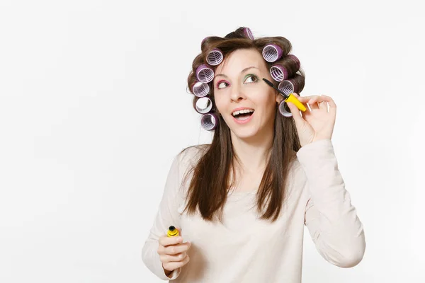 Fun young woman with curlers painting eyelashes with mascara isolated on white background. Crazy makeup with set facial decorative cosmetics. Beauty female fashion lifestyle concept. Area copy space. — Stock Photo, Image