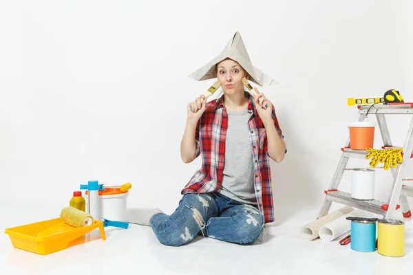 Szórakoztató nő ül a padló kefével, eszközök felújítás apartman szoba újság kalapban elszigetelt fehér background. Tapéta, kiegészítők, ragasztás, festés eszközök. Javítás otthon koncepció. — Stock Fotó