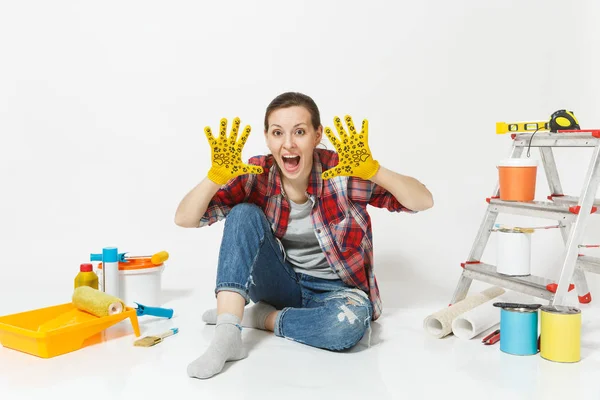 Διασκέδαση όμορφη γυναίκα σε casual ρούχα που κάθεται στο πάτωμα με τα κίτρινα γάντια, όργανα για διαμέρισμα ανακαίνιση που απομονώνονται σε λευκό φόντο. Ταπετσαρία αξεσουάρ για εργαλεία ζωγραφικής. Επισκευή concept home — Φωτογραφία Αρχείου